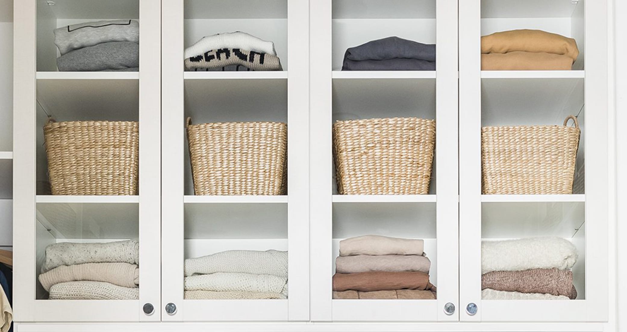 Glass cabinet doors display linen hallway closet storage in white wood grain finish by California Closets