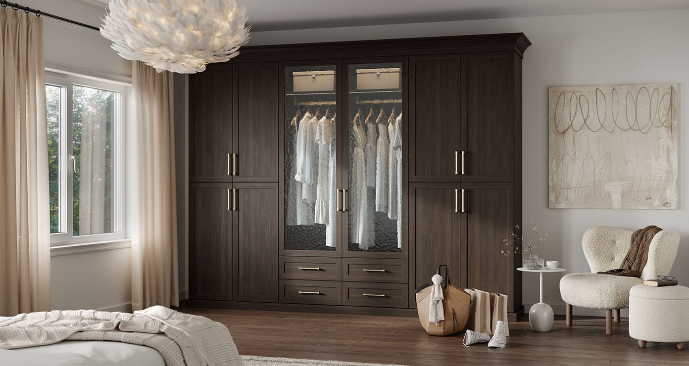 Wardrobe closet finished in dark wood grain with glass door cabinets and drawers by California Closets