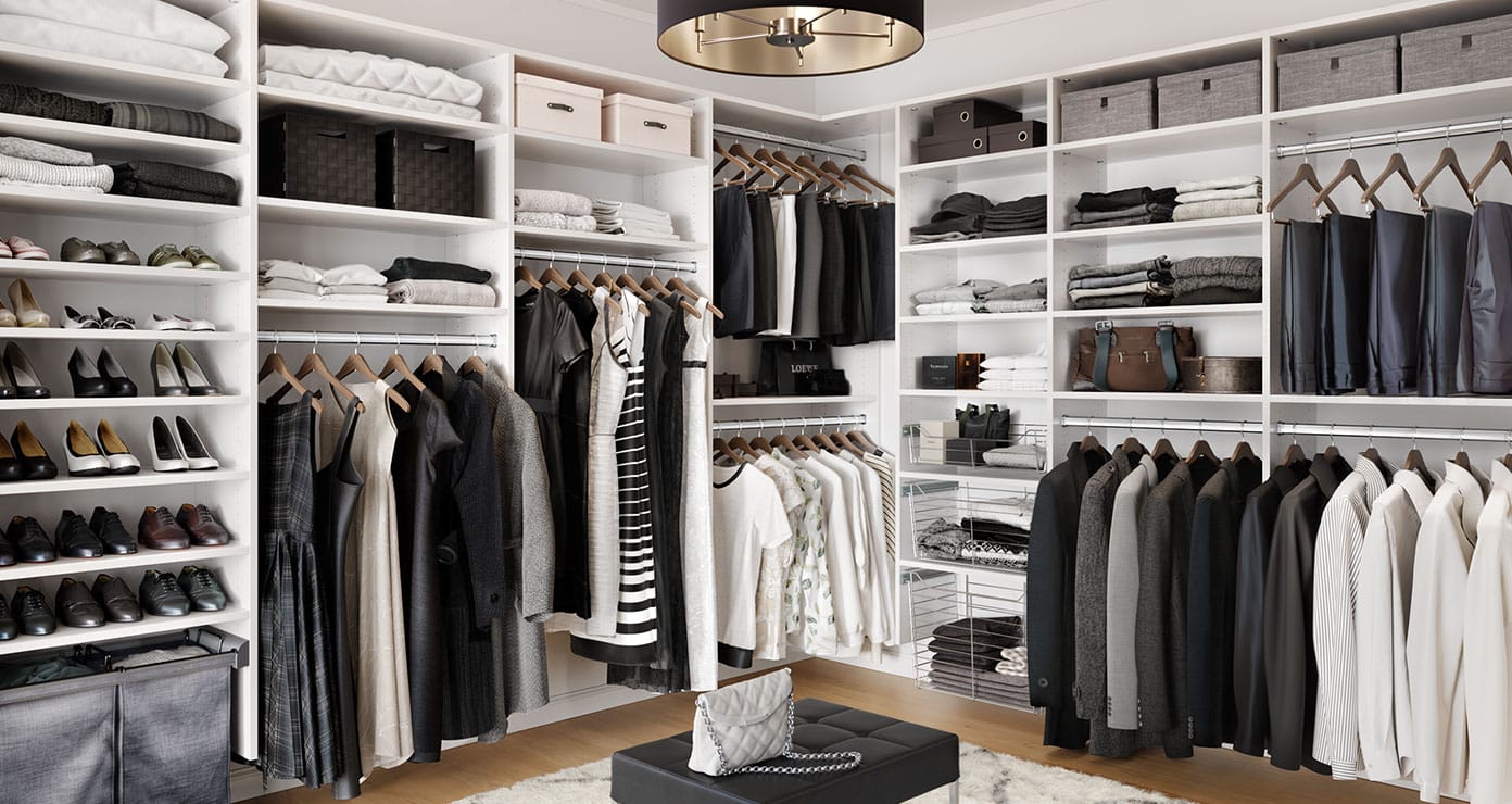 Walk in closet designed for his and hers wardrobe storage with center seating by California Closets